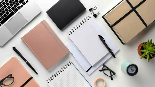 Flatlay of notebooks, pens, eyeglasses, and office accessories neatly arranged on a desk